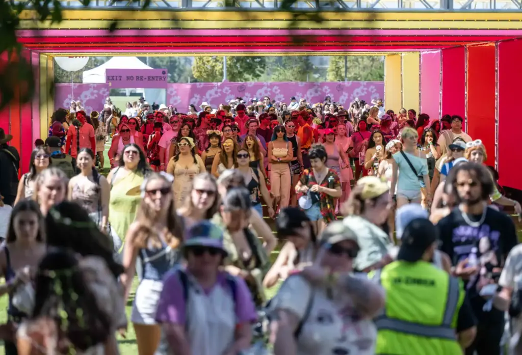 Thousands of festival goers walk through a rainbow tunnel as...