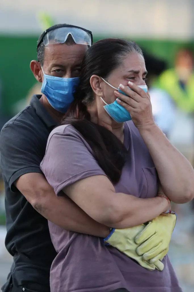 Residents embrace as rescue workers search through the rubble of their damaged home.