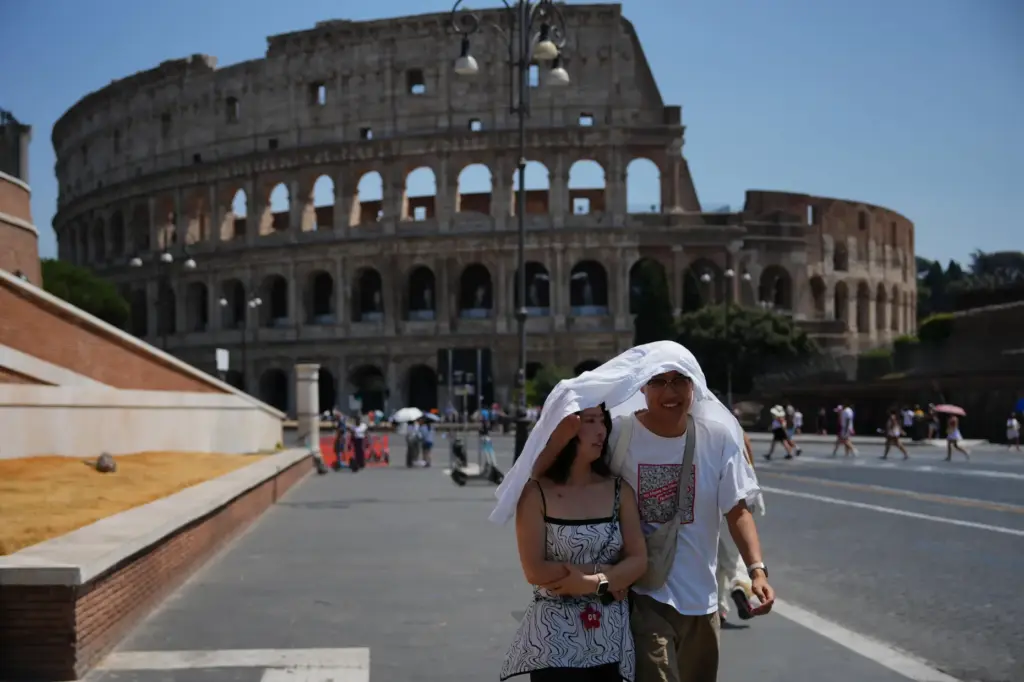 FILE – Tourists take shelter as they walk in front...