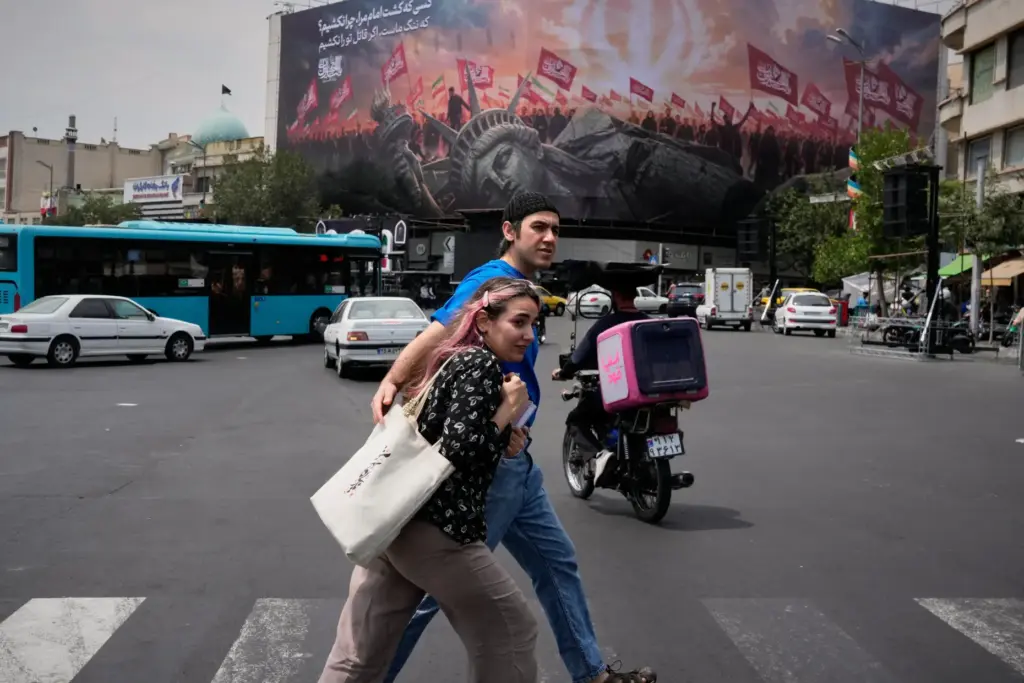 Pedestrians cross a street in front of a billboard depicting a fallen Statue of Liberty.