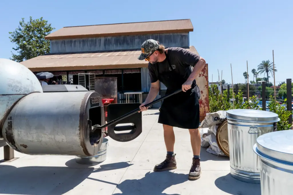 Daniel Payne adjusts fresh wood inside an offset smokerâs firebox...