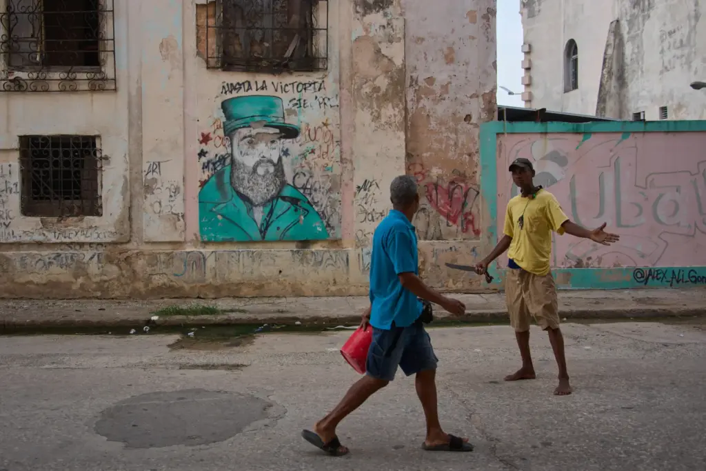 Men argue in front of a weathered mural of Fidel Castro in Havana, Cuba.