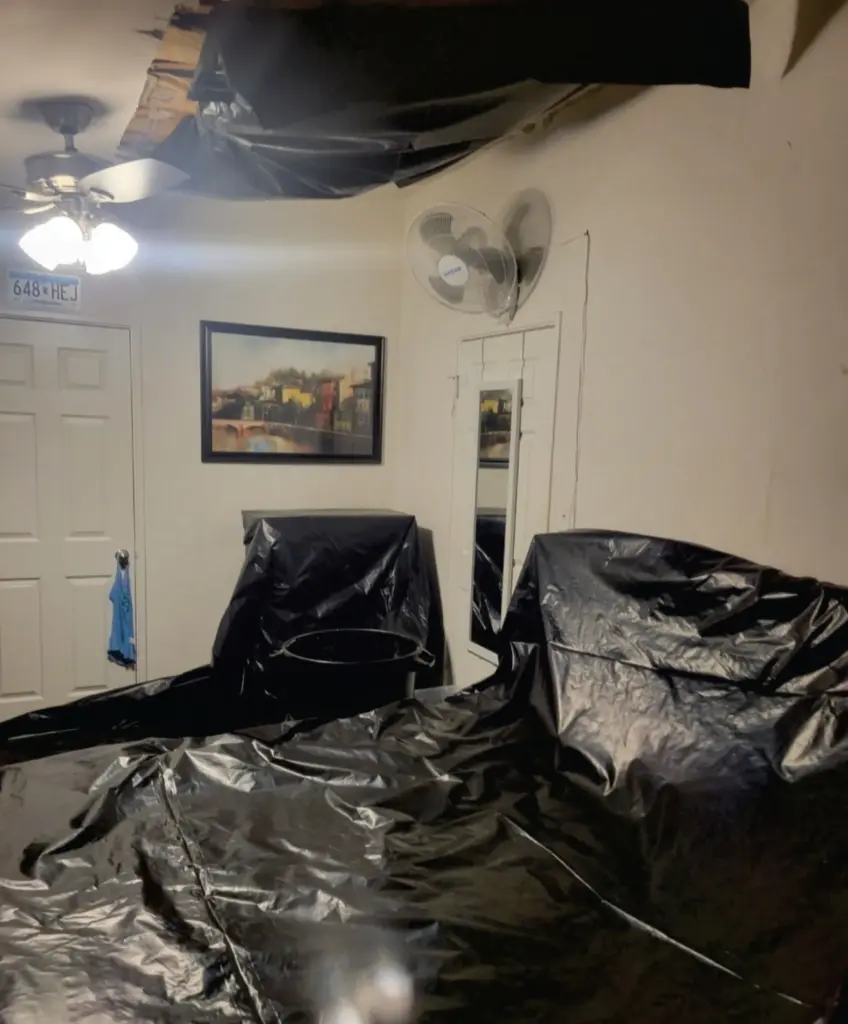 Black trash bags cover a caved-in ceiling and bedroom furniture.
