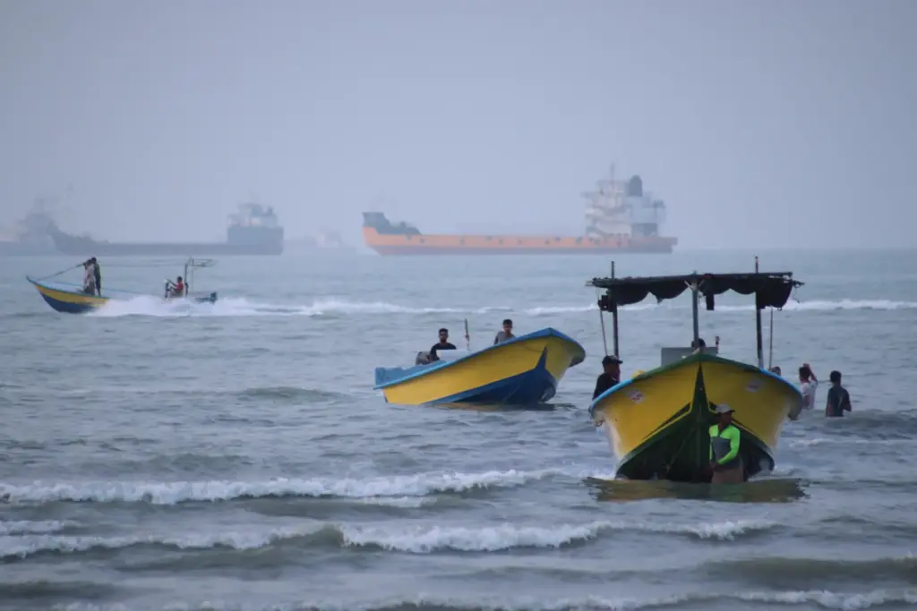 Small boats line the shore as cargo ships and other...