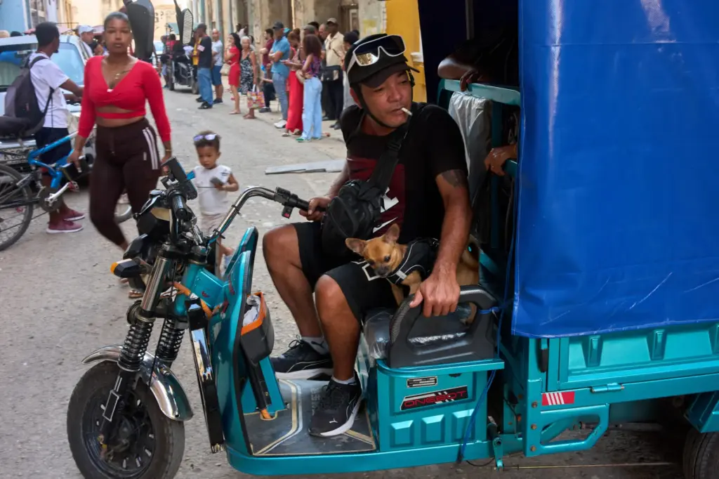 A man maneuvers his electric tricycle alongside his small dog in Havana, Cuba.