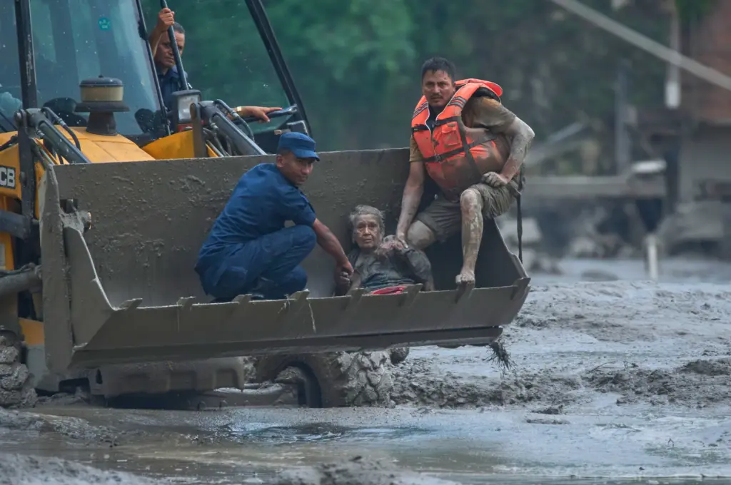 Rescuers use an earthmover to carry a victim of flash...