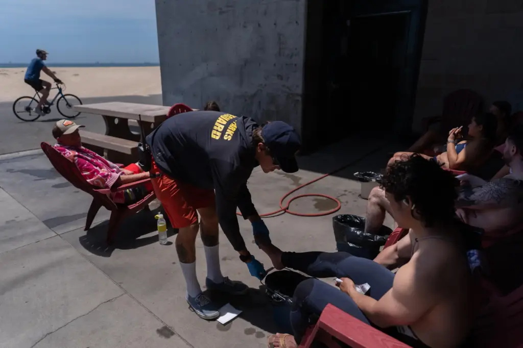 Lifeguard Max Voci, center, treats beachgoers for stingray stings at...
