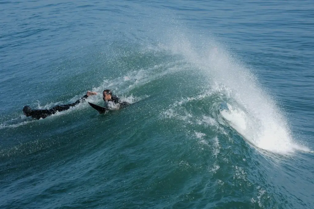 FILE – Surfers pass under a wave alongside the Imperial...