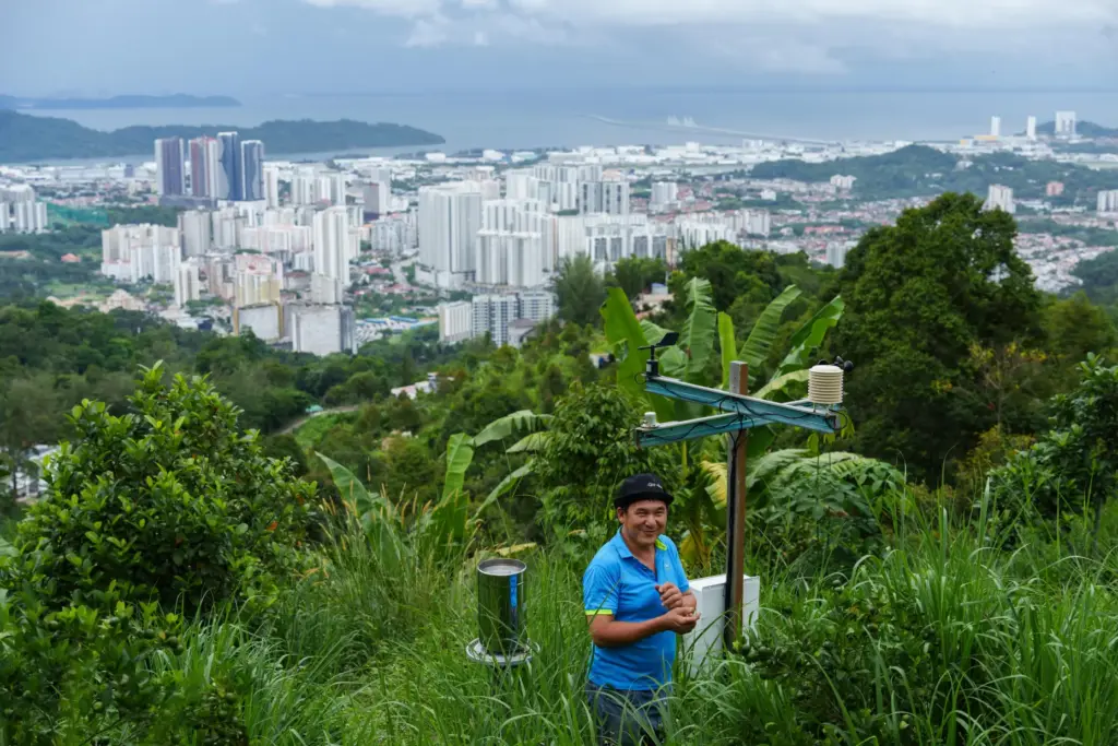 Durian farmer Kie Kim Hwa stands beside a weather and climate sensor station.