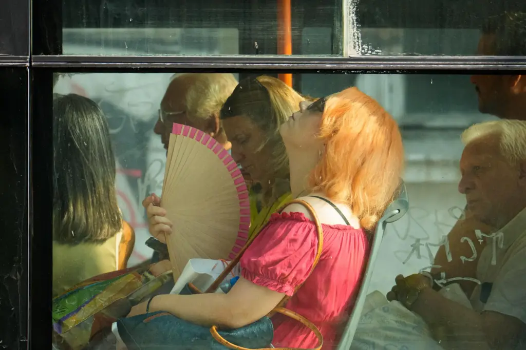 FILE – A woman uses a fan to cool off...