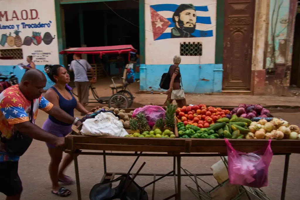Street vendors push their cart of vegetables past a mural...