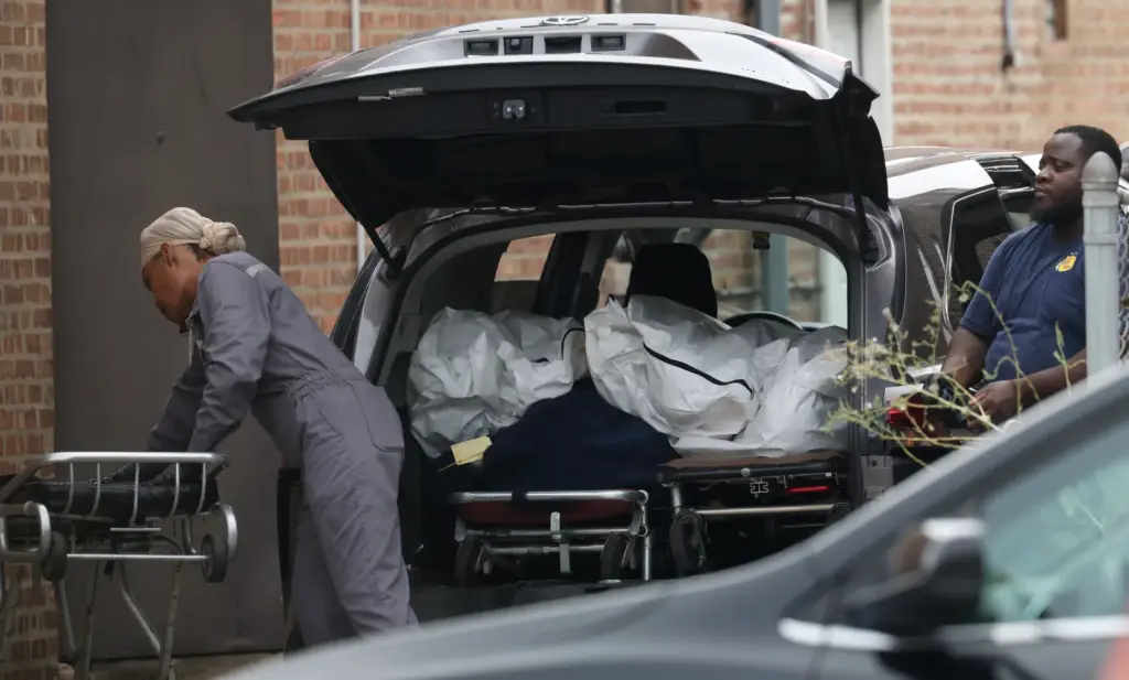 Workers load bodies Aug. 7, 2026, into a minivan from...