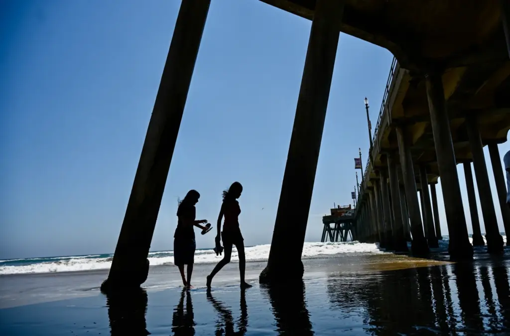 Beachgoers are silhouetted under the pier on Tuesday, August 11,...