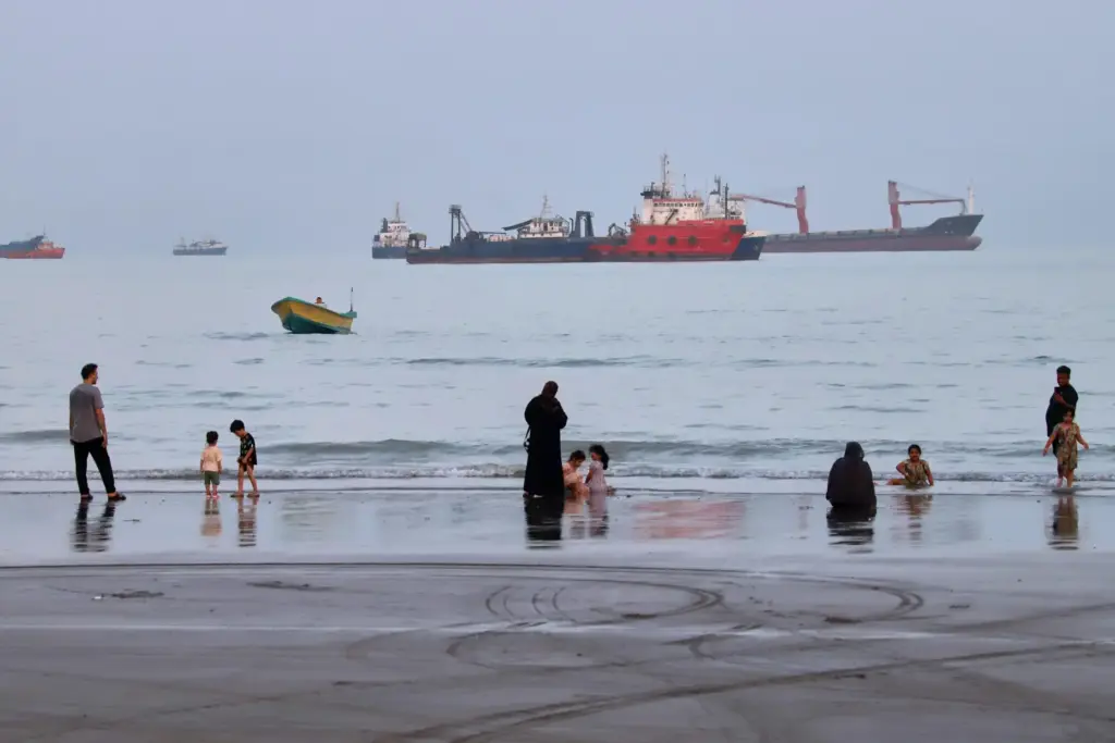 People spend time at a beach as commercial vessels are...