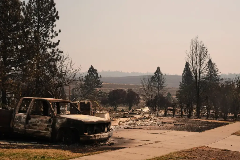 A burned truck sits in a driveway near several destroyed...