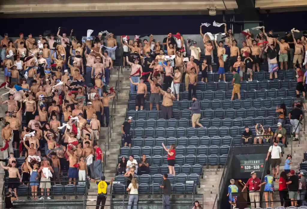 A group of young male fans wave their shirts in...