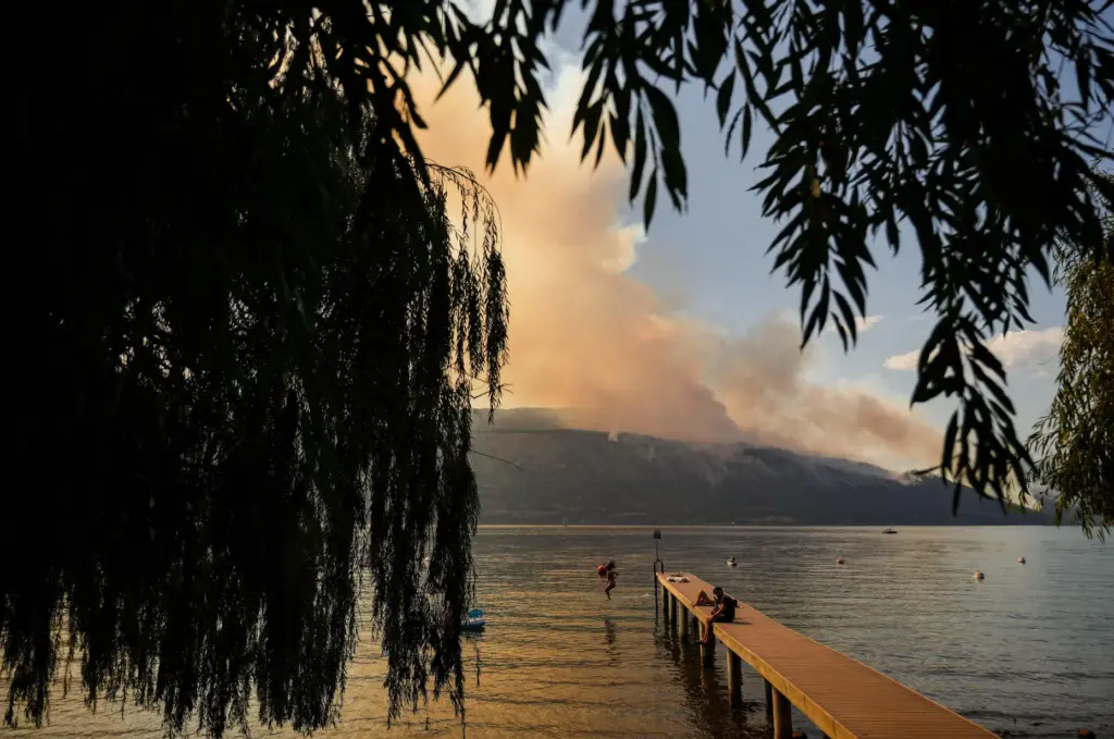 A woman jumps off a dock into Okanagan Lake as a wildfire burns.