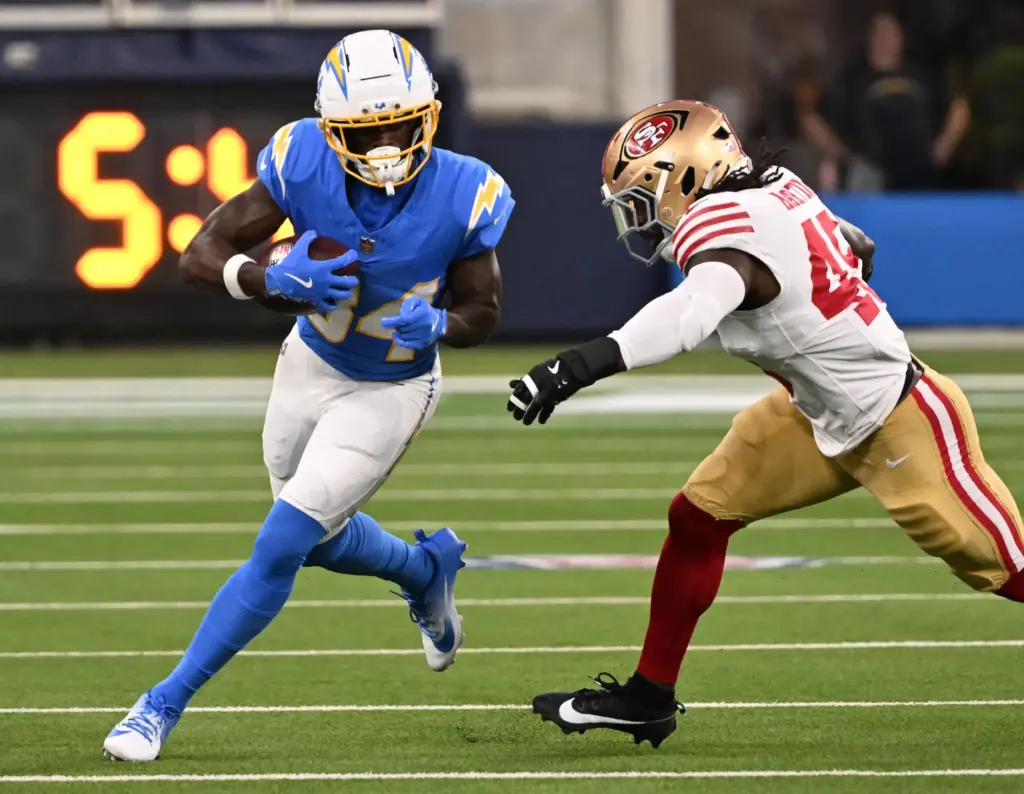 Chargers running back Keaton Mitchell, left, runs with the ball...