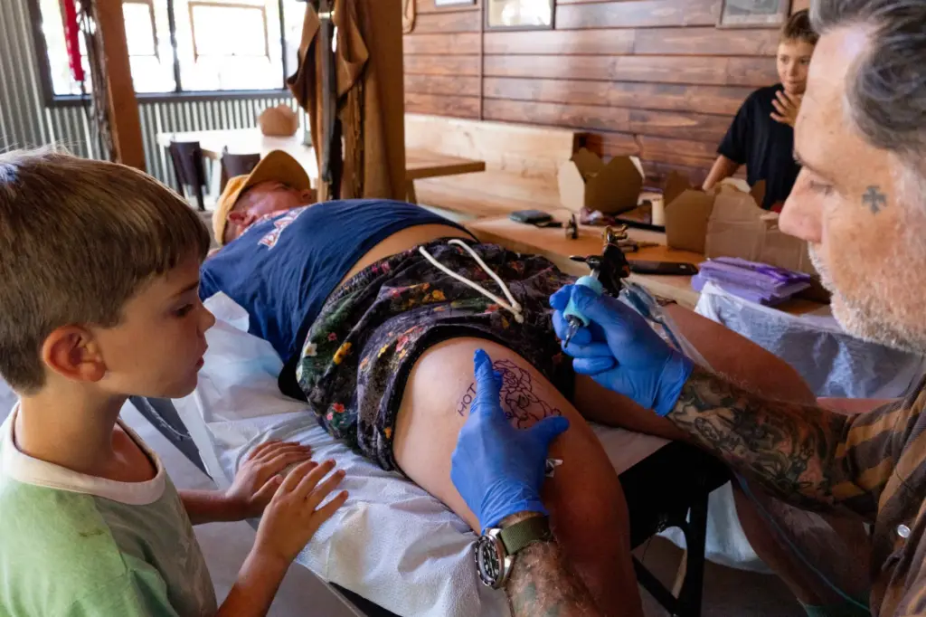 Eric Jones, right, inks a tattoo onto Marc Johnson, center,...