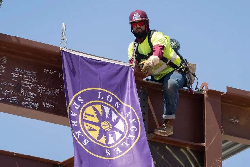 Crews raise and secure the final structural beam for the...