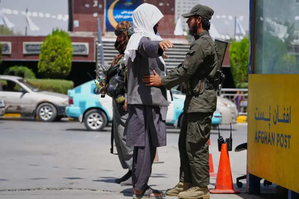 A Taliban security officer searches a man at a checkpoint...