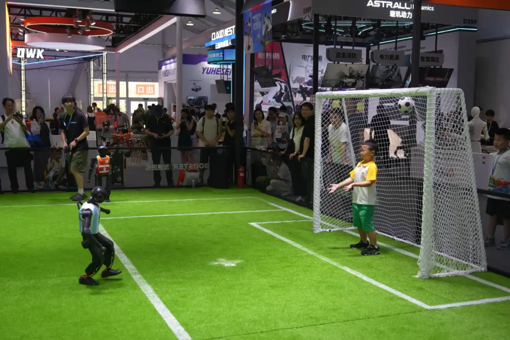 A child reacts as he plays soccer with a robot.