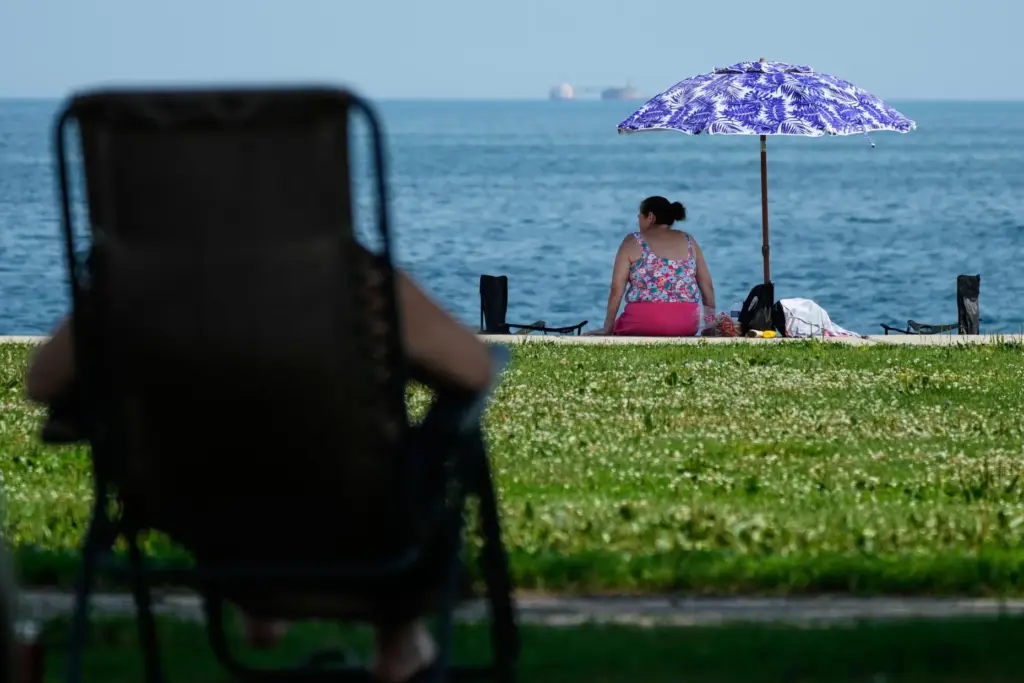 FILE – A woman cools off under a umbrella during...