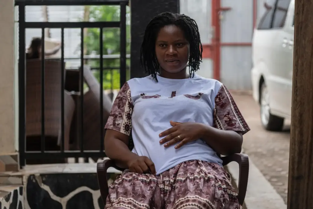 Esther Lutula sits outside her house.