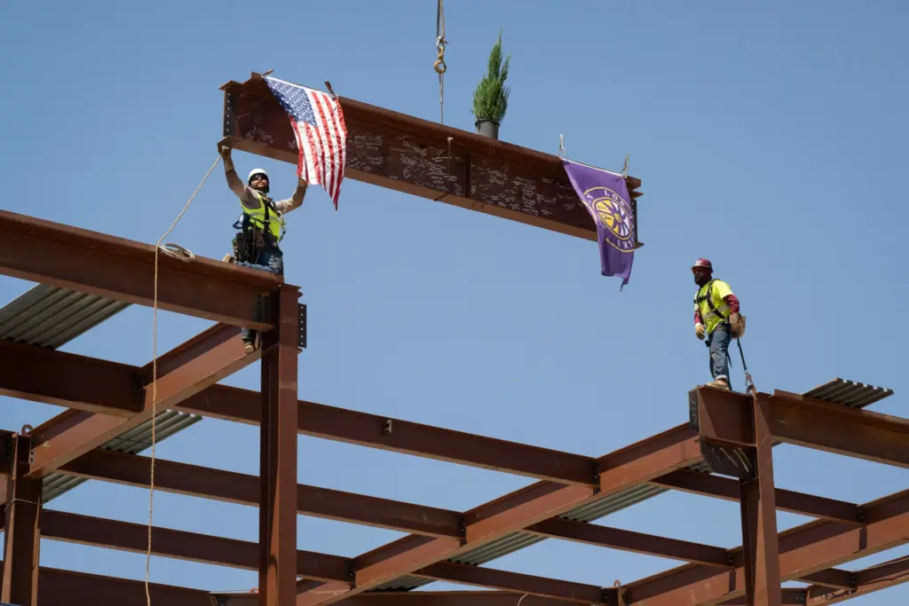 Crews raise and secure the final structural beam for the...