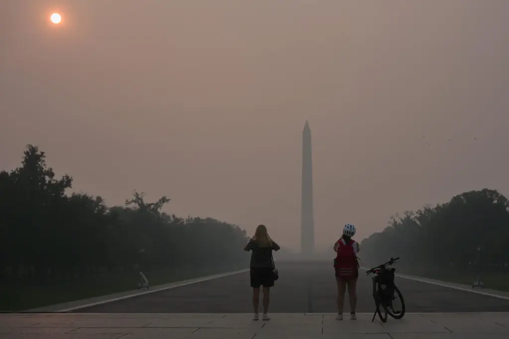 The sun is obscured by wildfire smoke as people stop to photograph the Washington Monument.