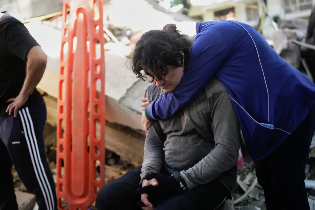 Neighbors embrace as rescue workers search through the rubble of a collapsed apartment building.