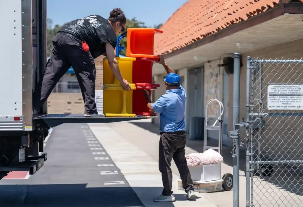 Custodial staff move age-appropriate furniture from a truck into a...