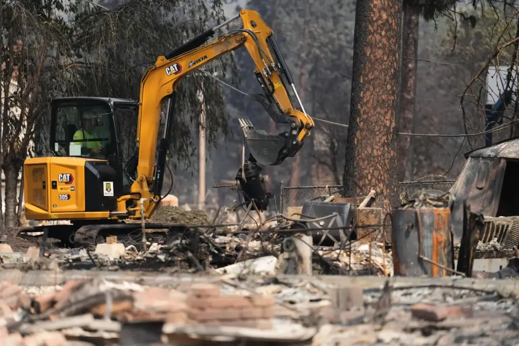 Crews work near several burned down houses after a wildfire...