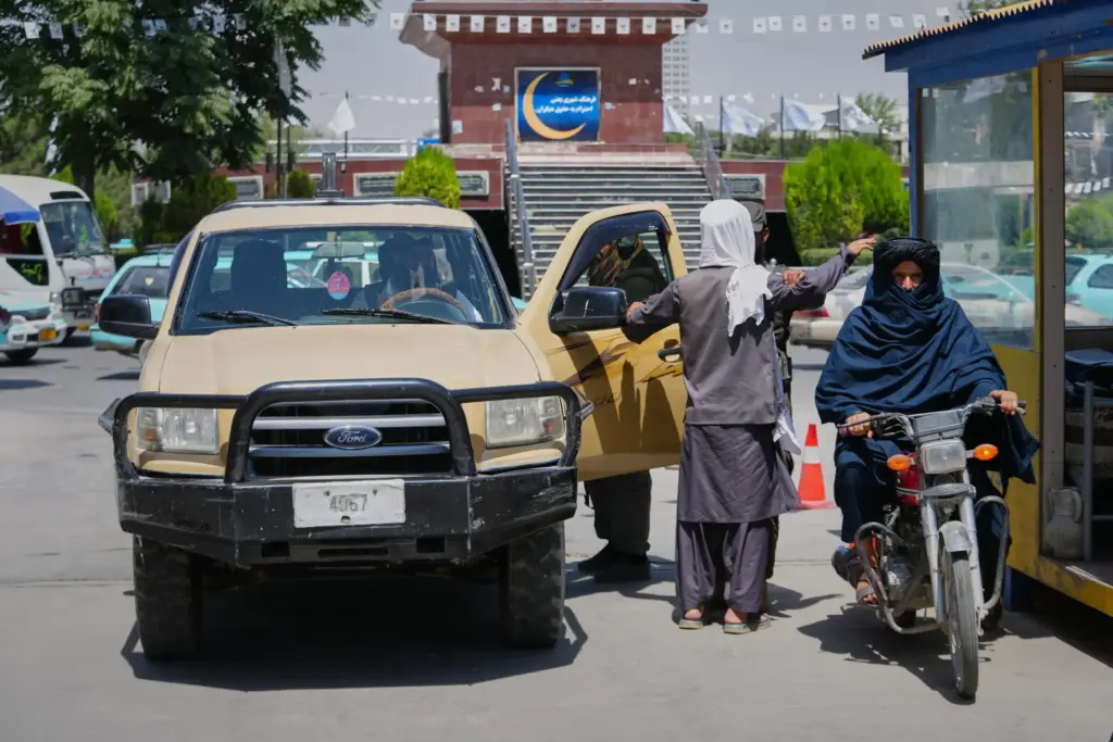 A Taliban security officer searches a man at a checkpoint...
