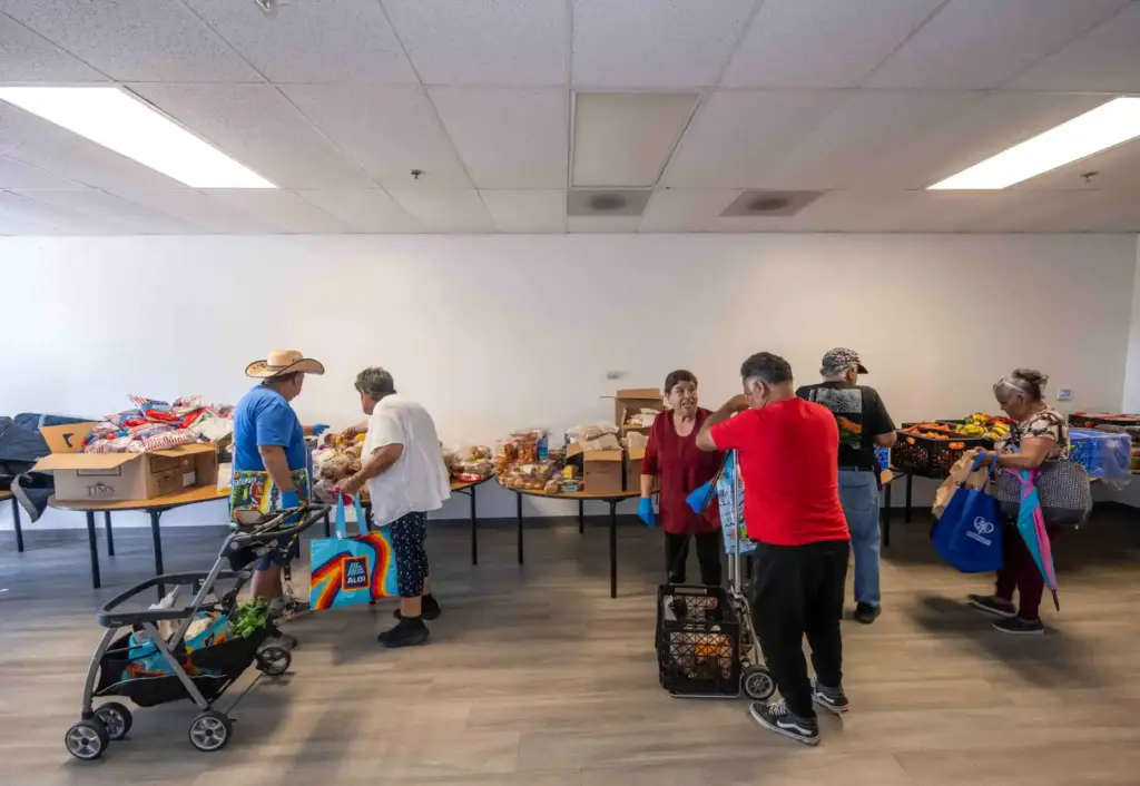 Volunteers help community members fill carts and baskets with food...