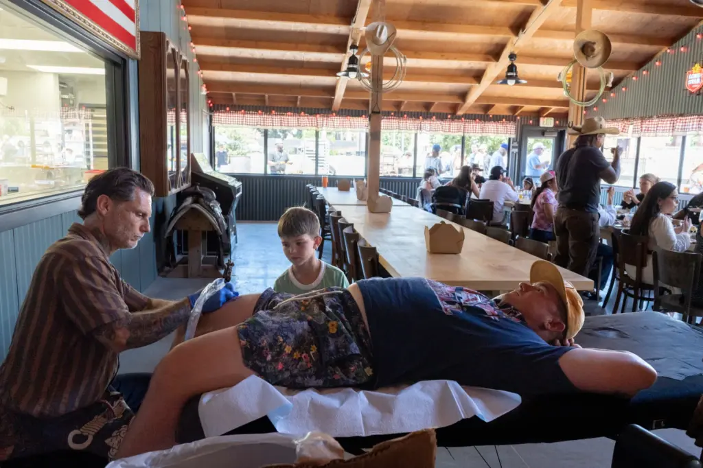 Eric Jones, left tattoos Marc Johnson while his son, Sonny,...