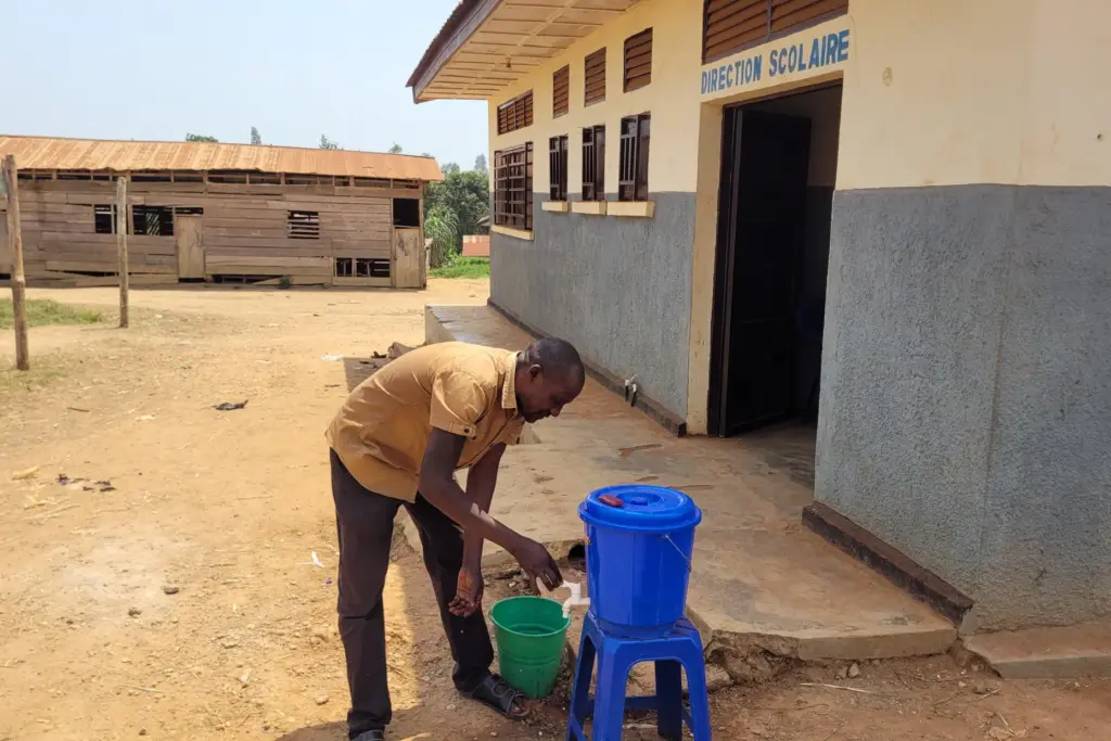 A parent who came for his child's school resumption washes his hands outside a school.