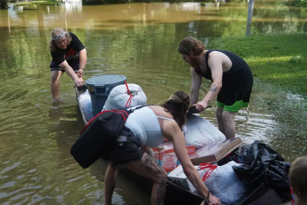 Scott Conrad, Joseph Workman and Kesley Patterson push a kayak through floodwaters.