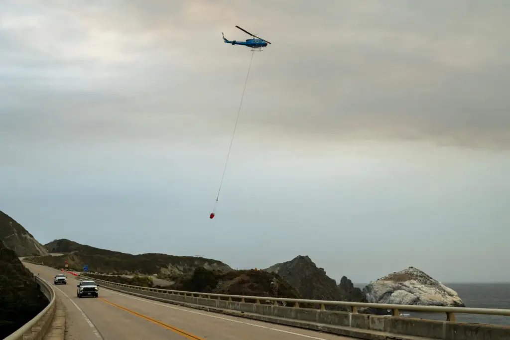 A helicopter flies over Willow Creek to fill up a water bucket.