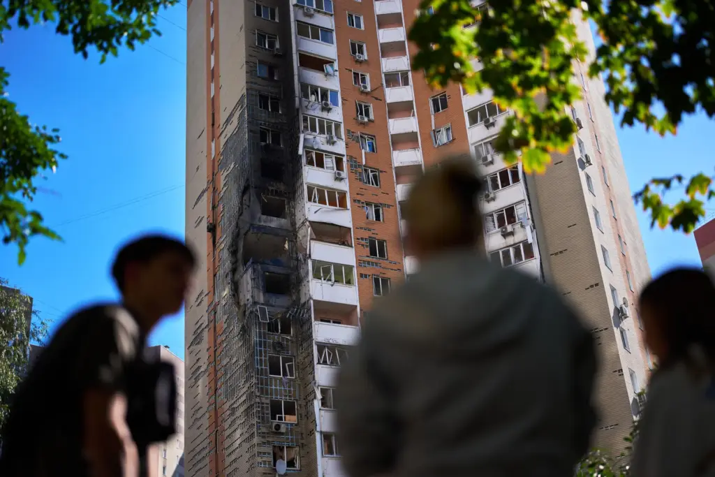 Locals watch as firefighters work on a partially damaged residential building following a Russian drone attack.