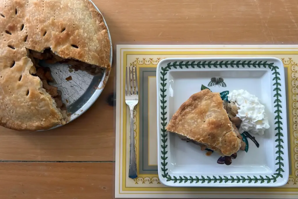 A freshly baked apple pie and a slice with whipped cream