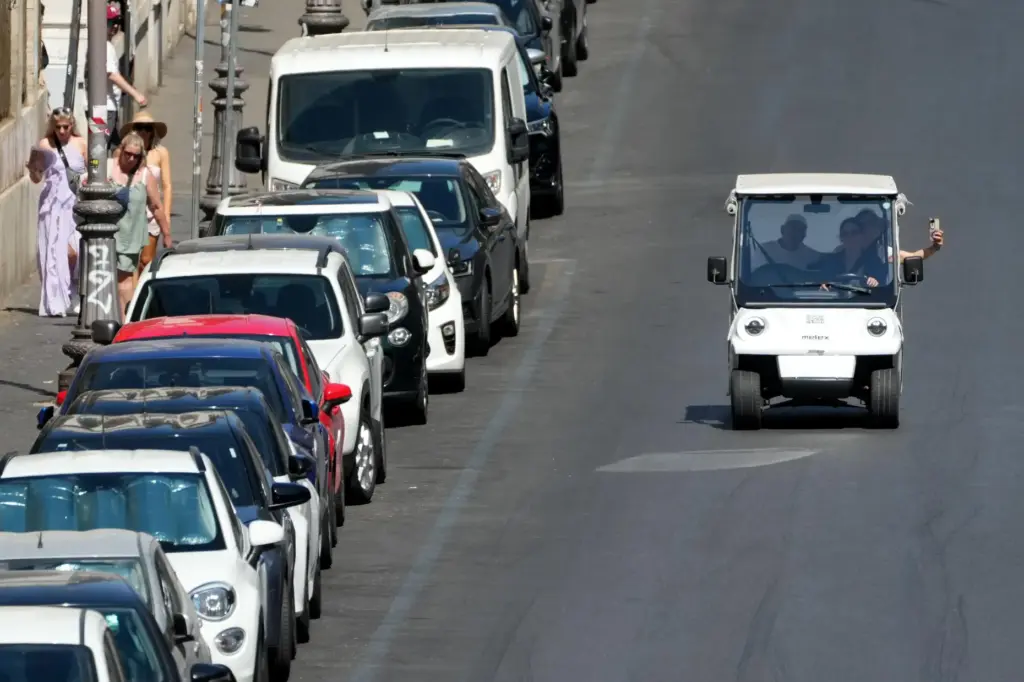 A golf cart carrying tourists travels past parked cars in Rome.