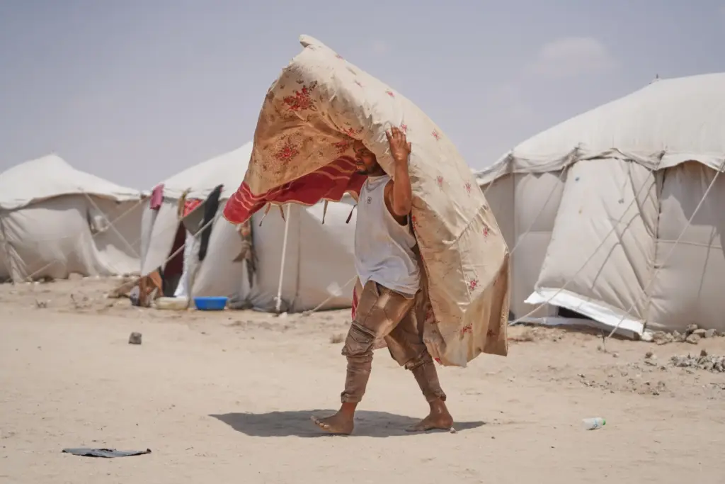 A displaced Yemeni carries a carpet at Al-Firdaws camp in Ras Imran.