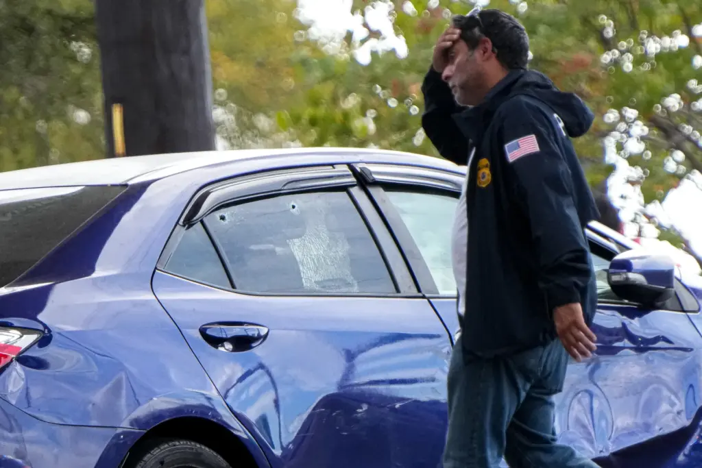 A federal agent walks past a vehicle with a damaged door and holes in the window.