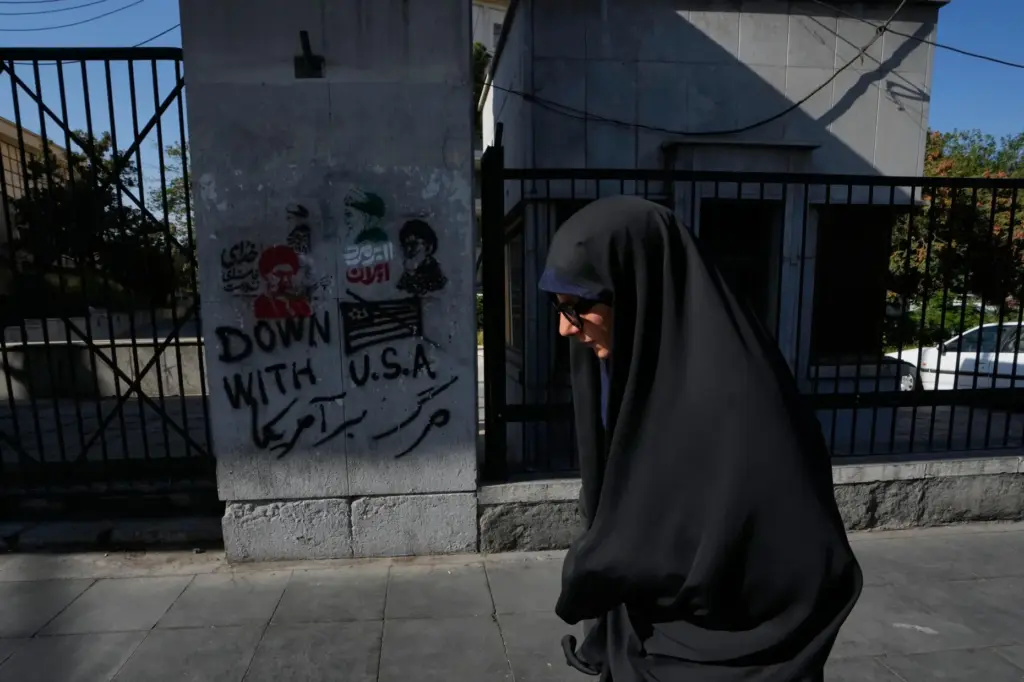 A woman walks past anti-U.S. graffiti and images depicting the...