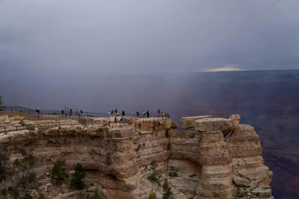People stand at the rim of the Grand Canyon as rain moves into the canyon.