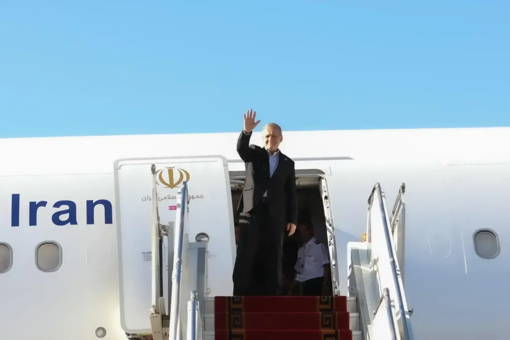 President Masoud Pezeshkian waves to media and officials as he boards his plane.