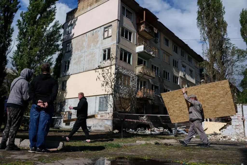 A municipal worker carries plywood to board up windows of...