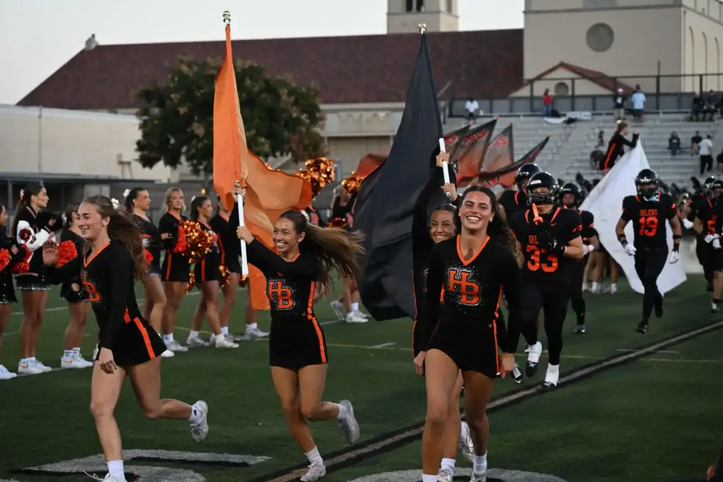 Huntington Beach Cheerleaders lead the football team on the field,...