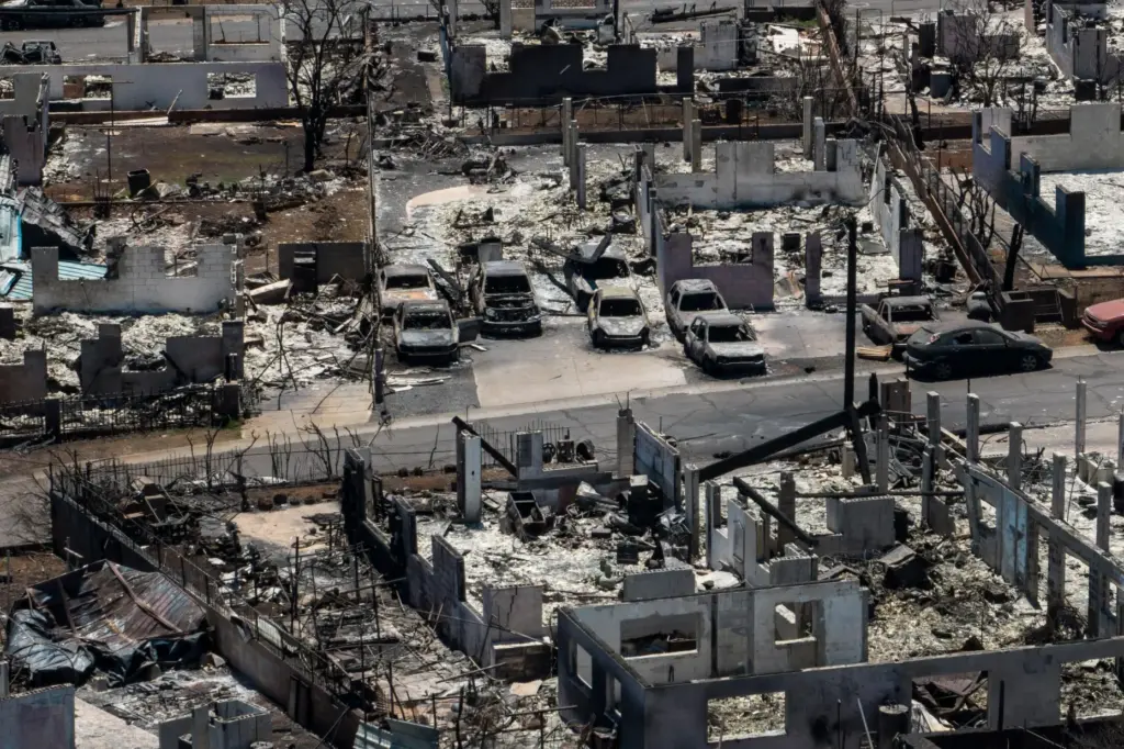 FILE – Charred vehicles remain near burned homes in the...